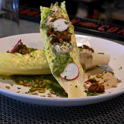 The image shows a plated dish with halved romaine lettuce, garnished with sauce, radish slices, herbs, and possibly some nuts or seeds on a white plate.