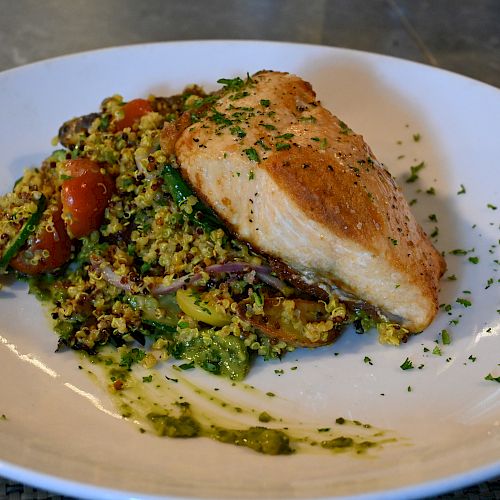 The image displays a plate of seared salmon served with a quinoa and vegetable medley, garnished with herbs on a white dish.